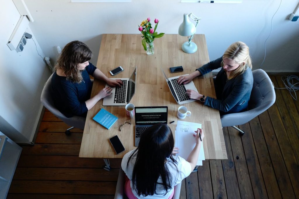 three women sitting around table using laptops